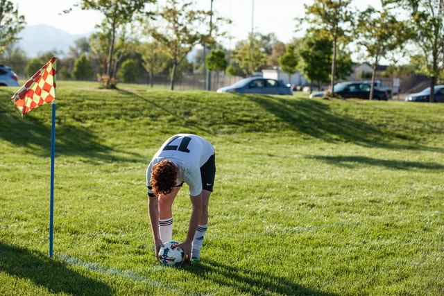 man in white shirt placing soccer ball on grass